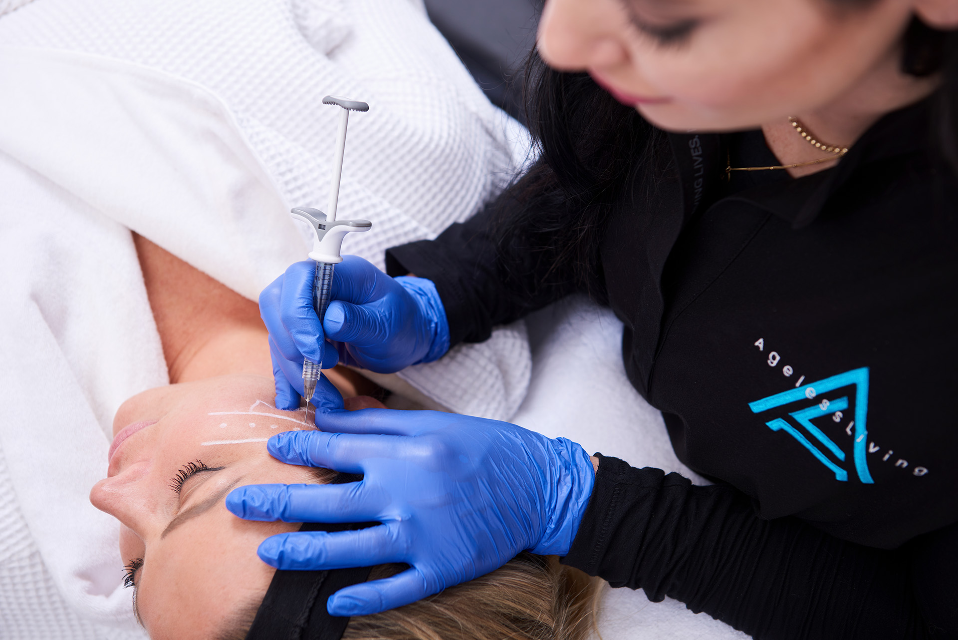 An Ageless Living injector treating a patient’s forehead, the area mapped out in white pencil